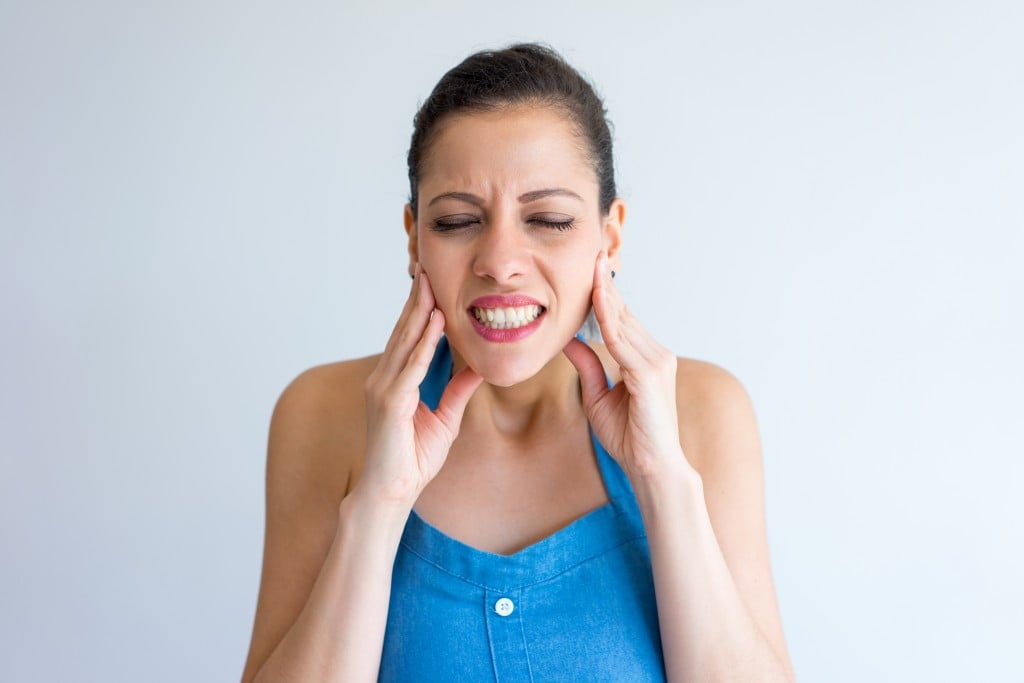 Annoyed young woman suffering from bruxism and touching jaw. Irritated girl with closed eyes gritting teeth from pain.