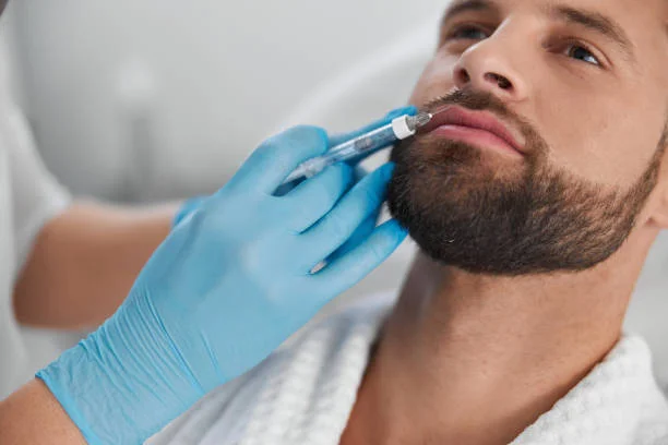 Attractive middle aged man with stylish beard undergoes contemporary lip augmentation procedure with cosmetologist doing injection in clinic closeup